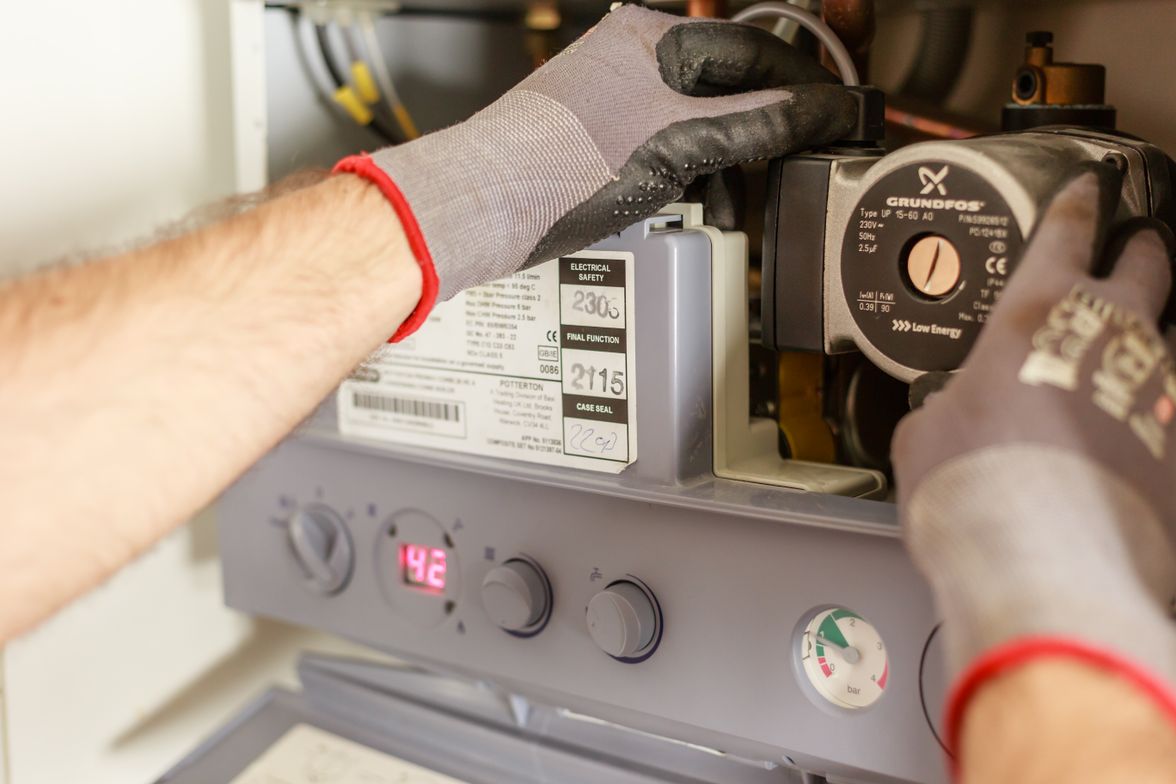 Gloved hands adjusting the circulator pump and controls on a residential boiler.