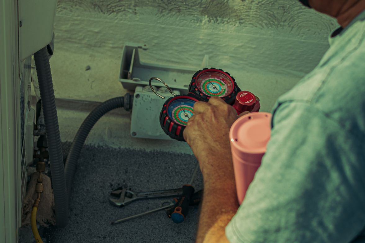 HVAC technician checking an outdoor air conditioning unit with service gauges connected.